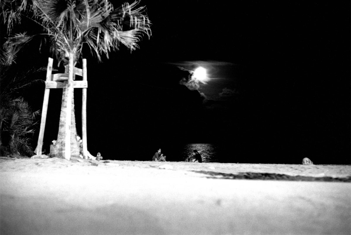 Tre persone conversano sulla spiaggia di notte davanti al riflesso della luce della luna
