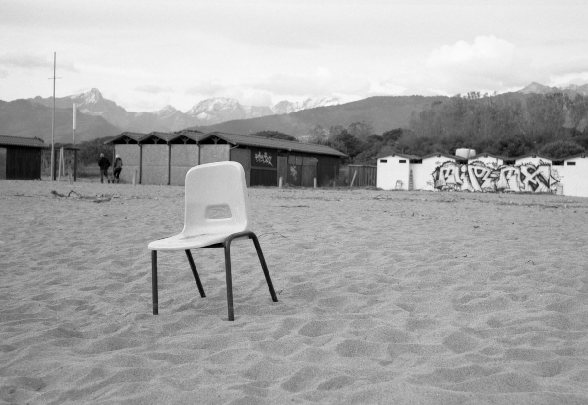 Sedia vuota sulla spiaggia del Cinquale in inverno con cabine, murales e Apuane sullo sfondo
