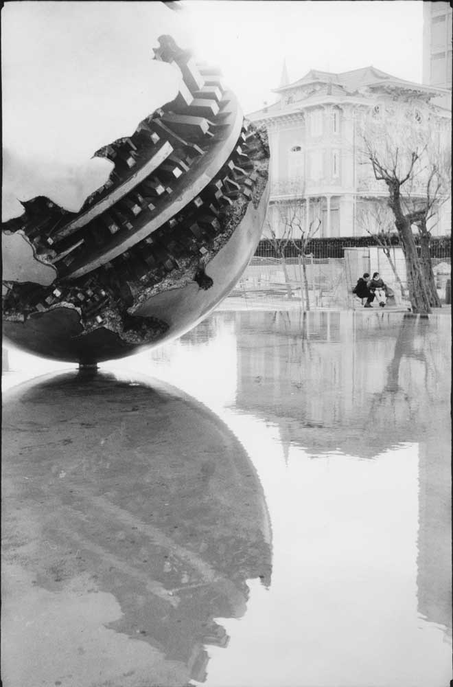 Fontana con opera di Arnaldo Pomodoro a Pesaro con persone sulla panchina sullo sfondo